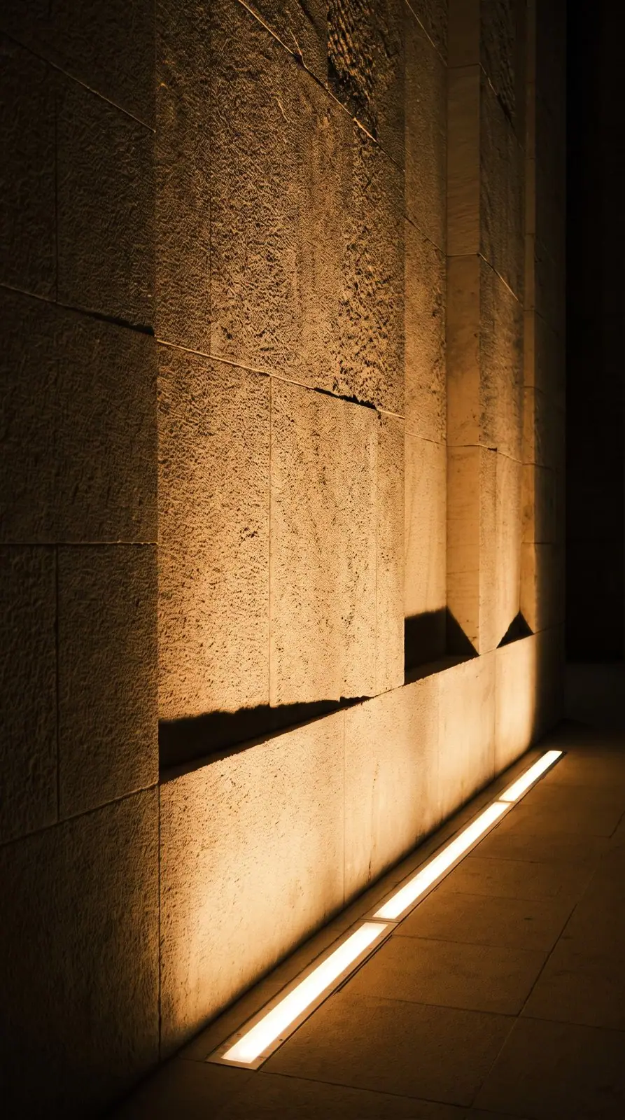 Linear luminaire grazing warm light up a sandstone facade at night
